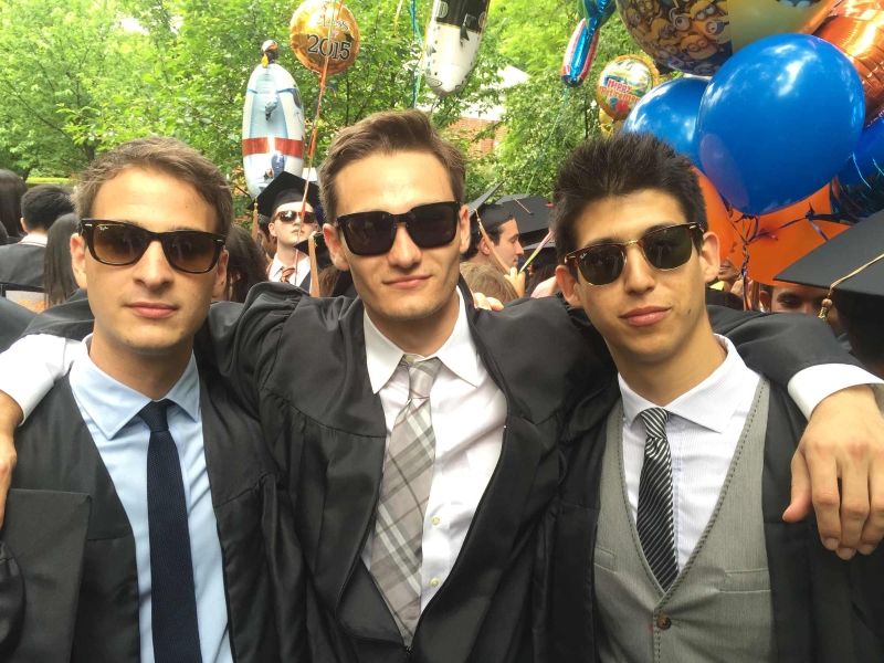 Three people in gowns and black glasses pose for a photo during a graduation celebration